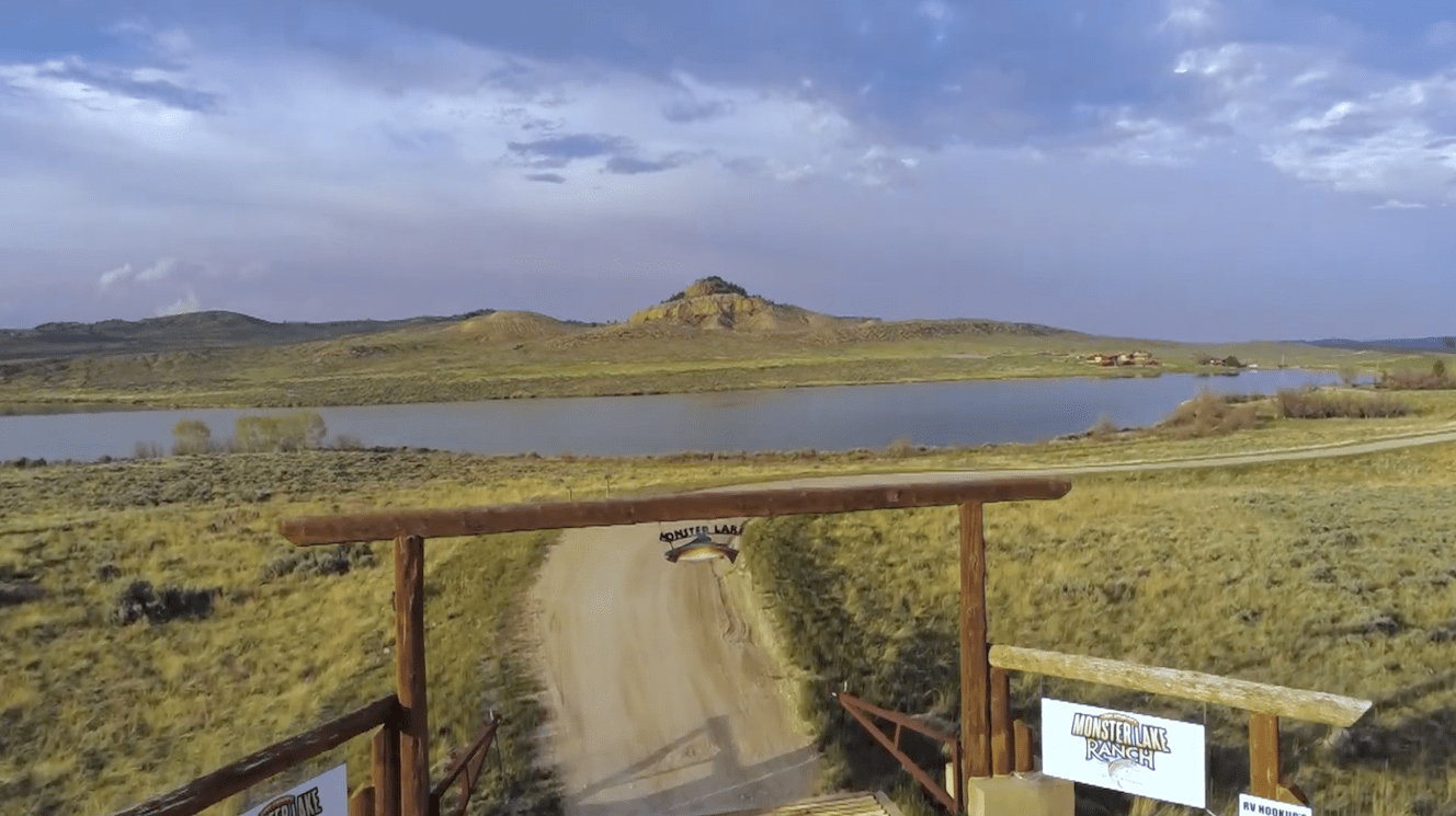A wide-angle view of the entrance to Kanye West's Wyoming ranch, featuring a long driveway and rustic gates surrounded by open plains.