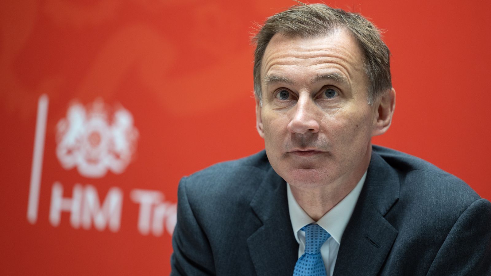 Jeremy Hunt looking thoughtful in front of an HM Treasury sign, reflecting on economic and fiscal matters.