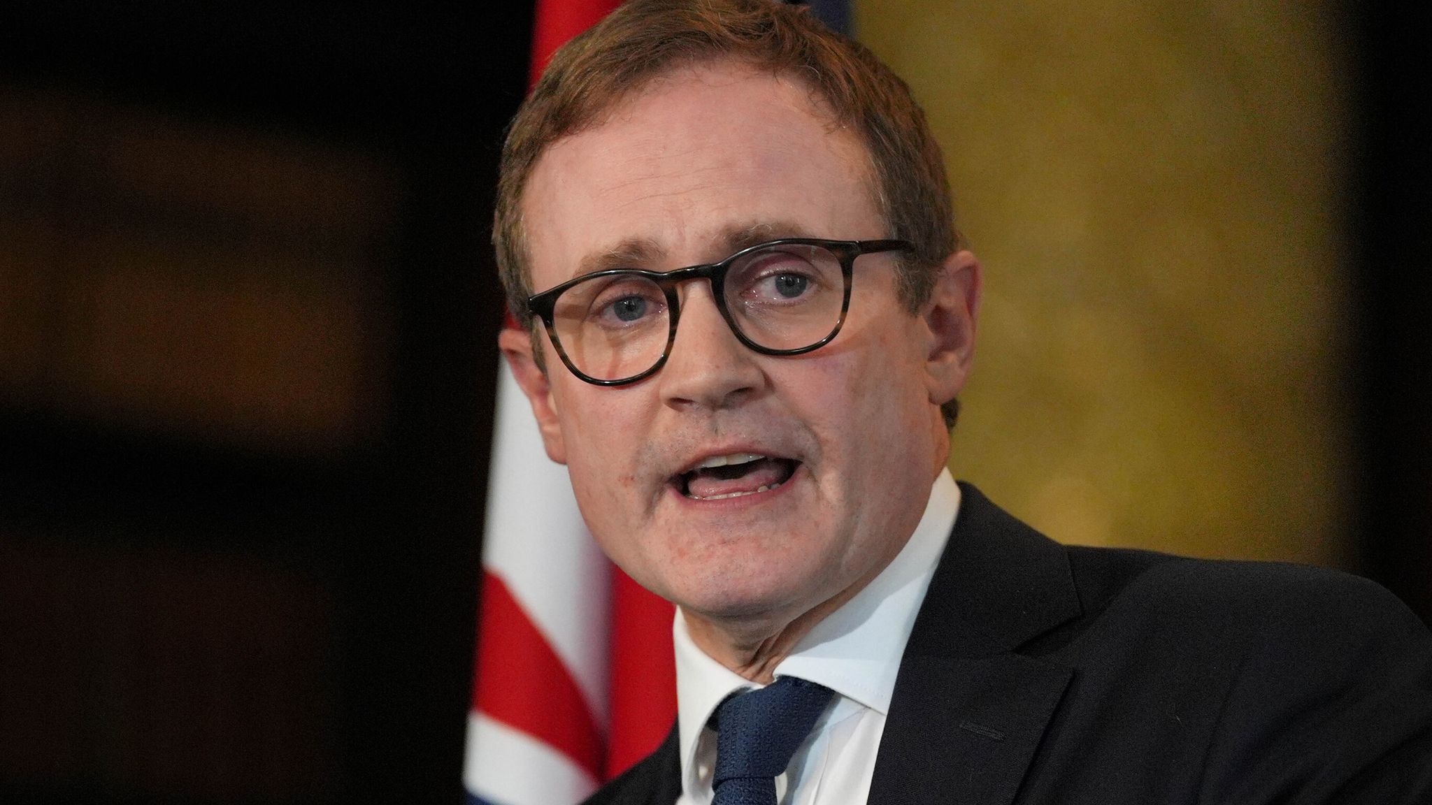 Tom Tugendhat giving a speech with the Union Jack flag displayed prominently behind him.