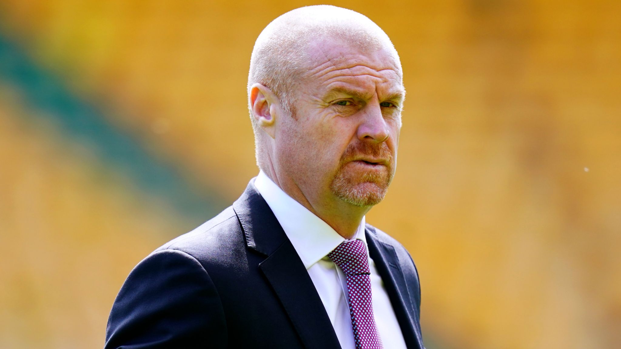 Sean Dyche standing in a football stadium wearing a tailored suit, looking focused and professional.