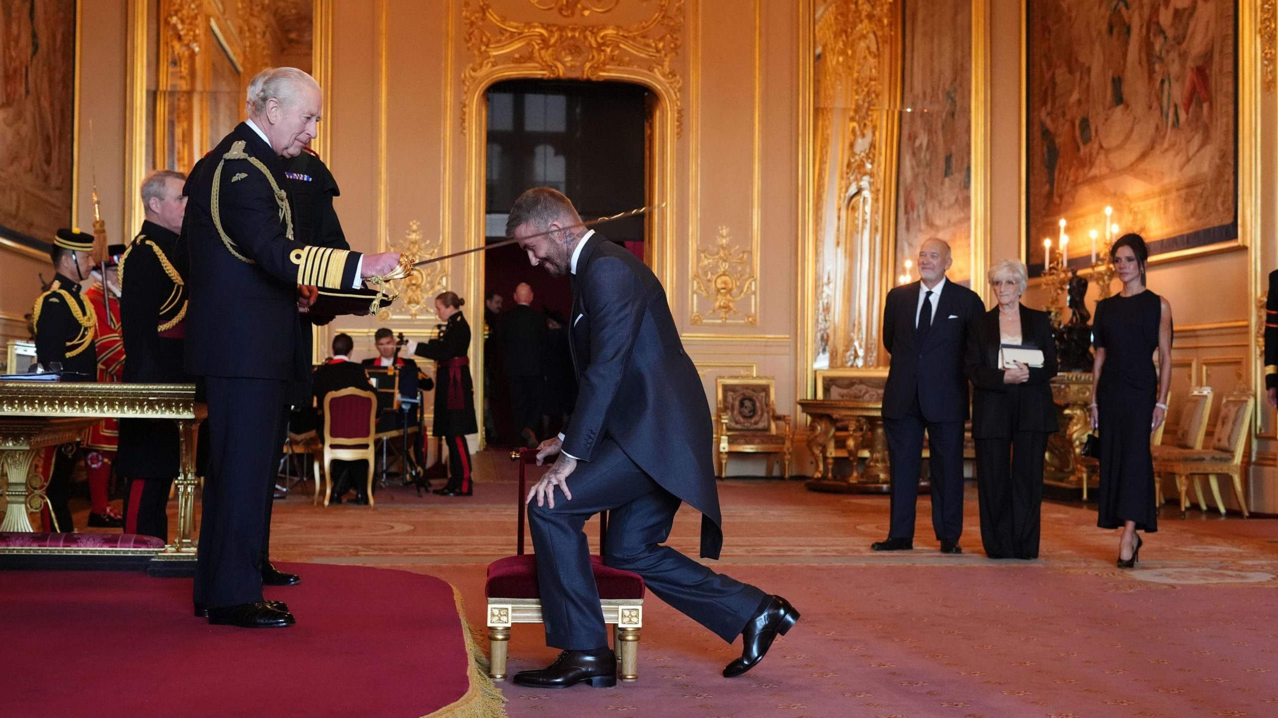 David Beckham bending down as King Charles confers a knighthood upon him at Windsor Castle.