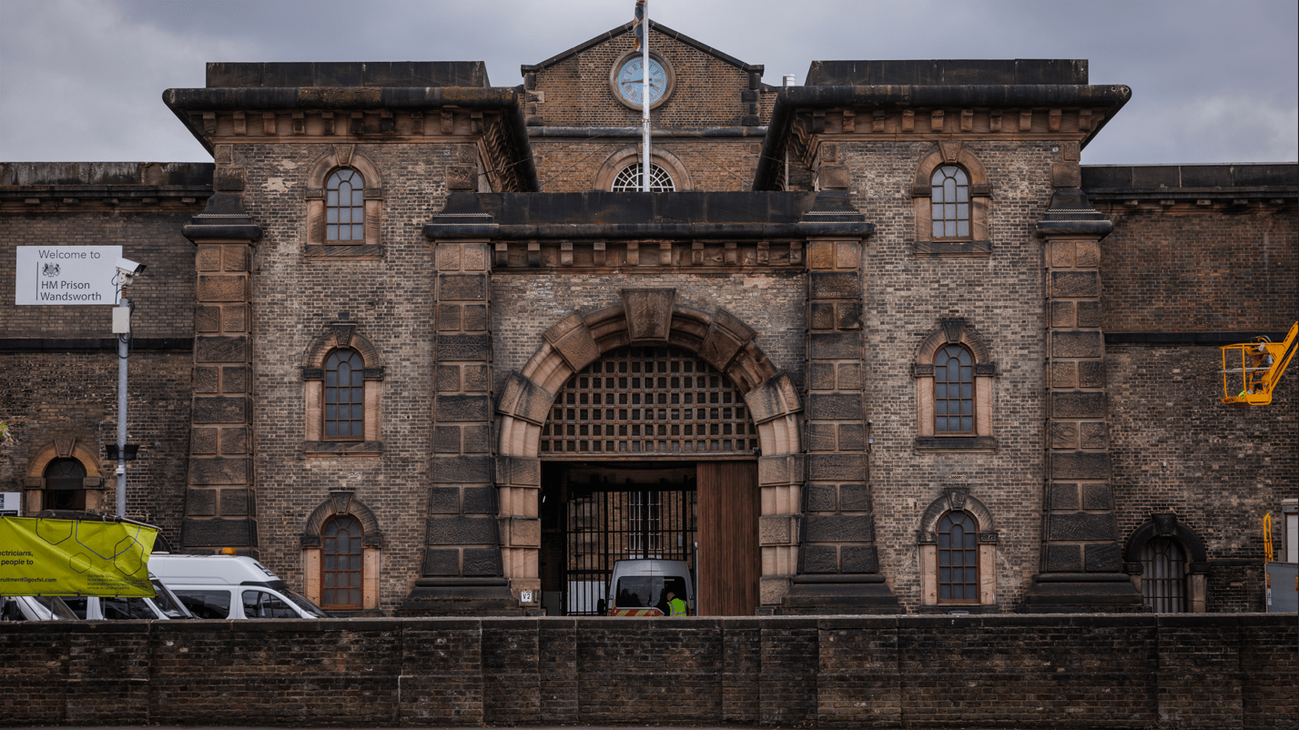 The front gate of HMP Wandsworth, surrounded by security fencing and guarded entrances, standing at the centre of the growing prison scandal.