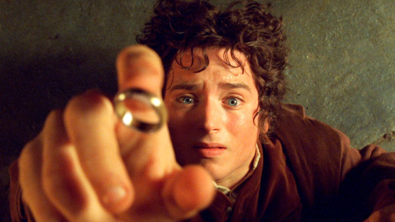 Elijah Wood as Frodo Baggins, reaching out toward the One Ring with a tense expression, capturing the pivotal moment of temptation in The Lord of the Rings.