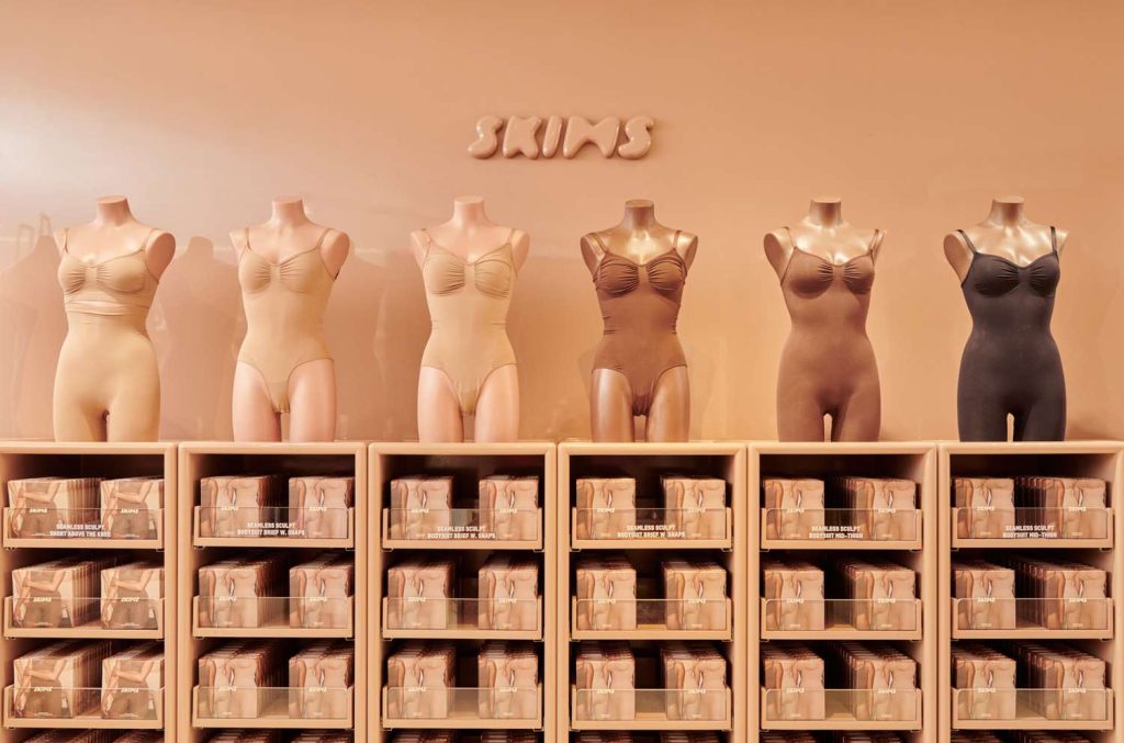 Display of Skims shapewear on mannequins in a retail store, showing inclusive skin-tone color range and neatly organized product shelves