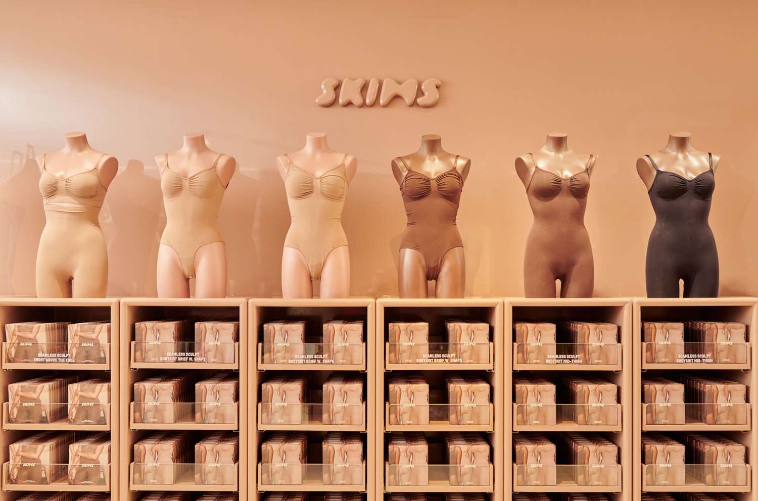 Display of Skims shapewear on mannequins in a retail store, showing inclusive skin-tone color range and neatly organized product shelves