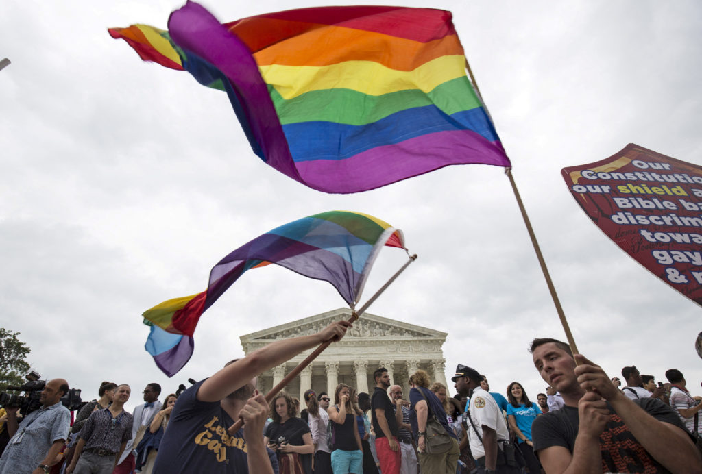 Crowd of LGBTQ+ supporters waving rainbow Pride flags outside the U.S. Supreme Court.