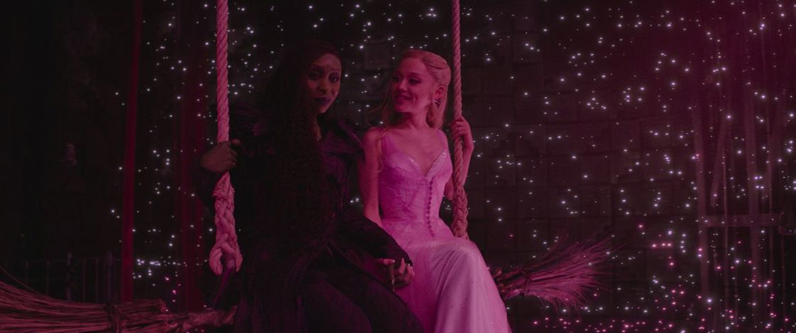 Ariana Grande as Glinda and Cynthia Erivo as Elphaba sitting on a swing in character during an emotional scene from Wicked: For Good.