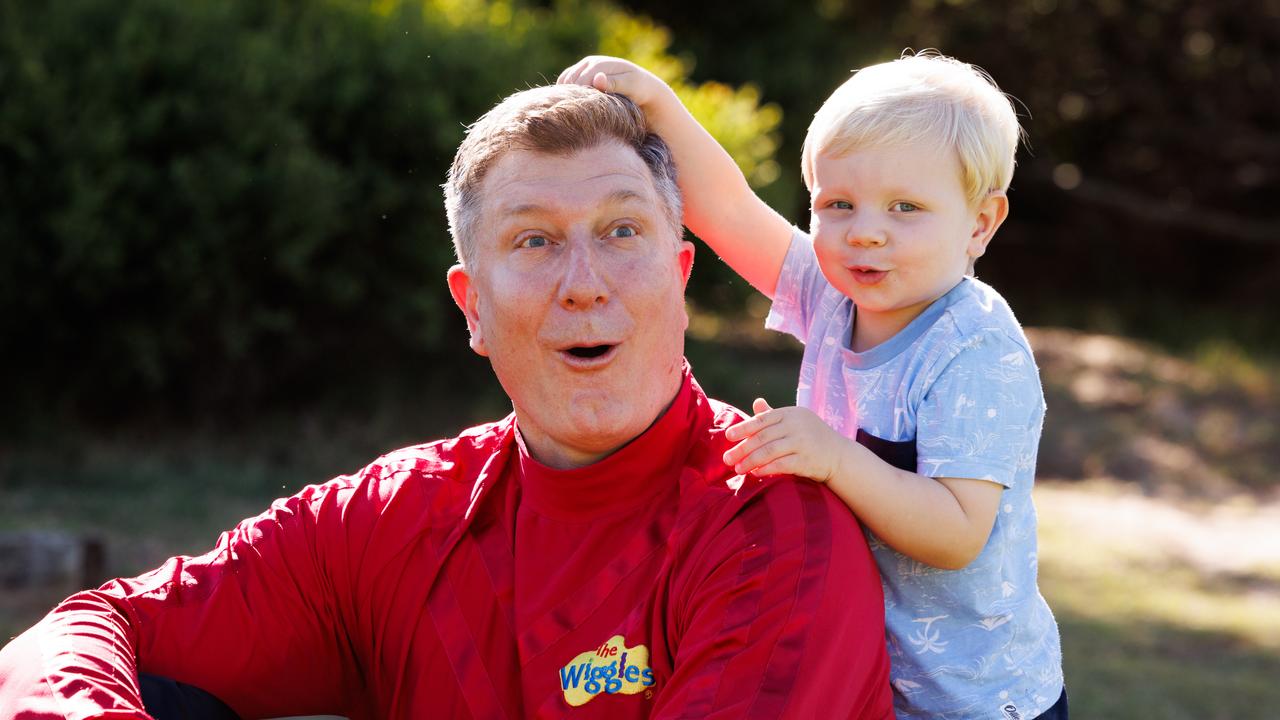Simon Pryce wearing his Red Wiggle outfit, smiling and playing with a young child during a performance.