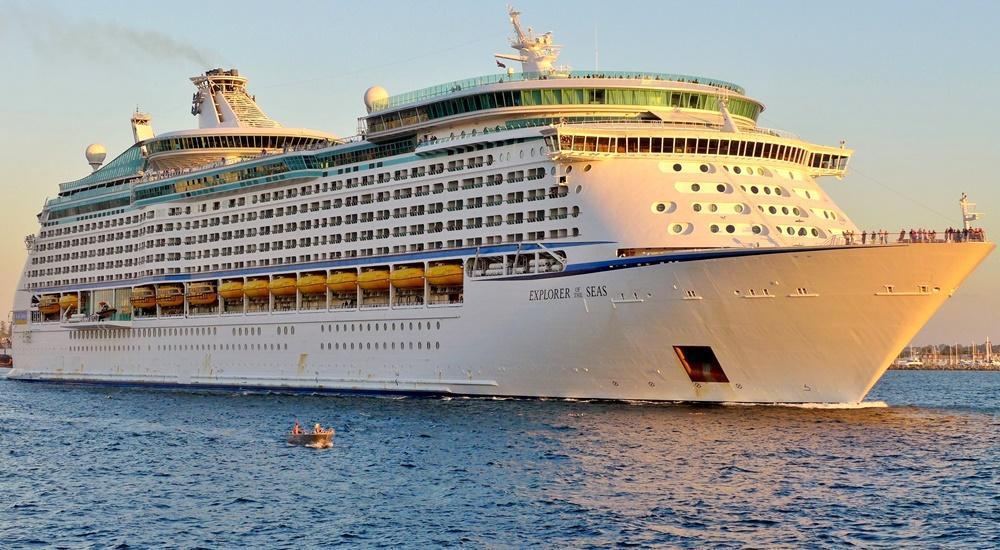 The Explorer of the Seas cruise ship docked in the Caribbean, with its signature blue hull and sunlit decks visible under clear skies.