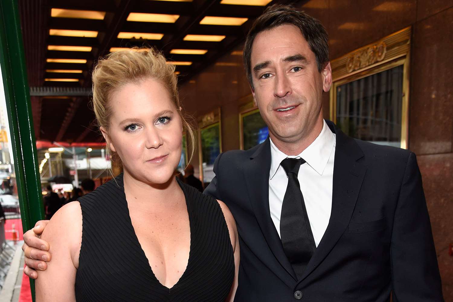 Amy Schumer and Chris Fischer dressed in black, looking glamorous at a formal event, reflecting the couple during happier times before divorce rumors emerged.