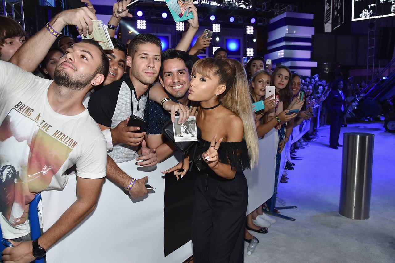 Ariana Grande smiling and taking selfies with fans on the red carpet a few years ago, engaging warmly with her audience.