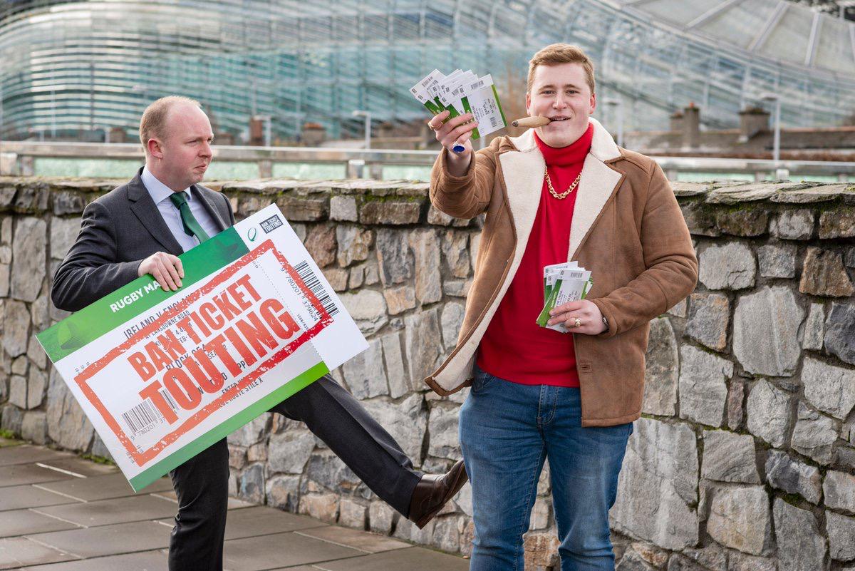 A protester holding a sign that reads “Ban Ticket Touting” and gesturing toward a person symbolically representing a ticket tout.