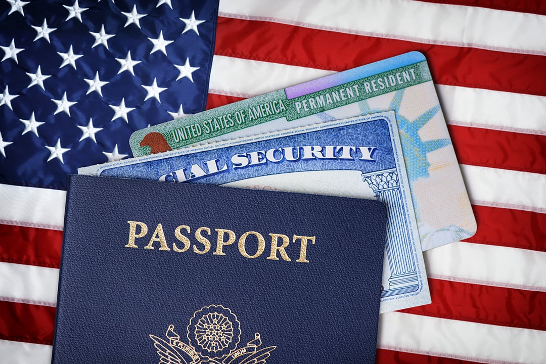 A U.S. passport and green card placed on top of an American flag, highlighting the tension surrounding citizenship, immigration status, and new federal policy shifts.