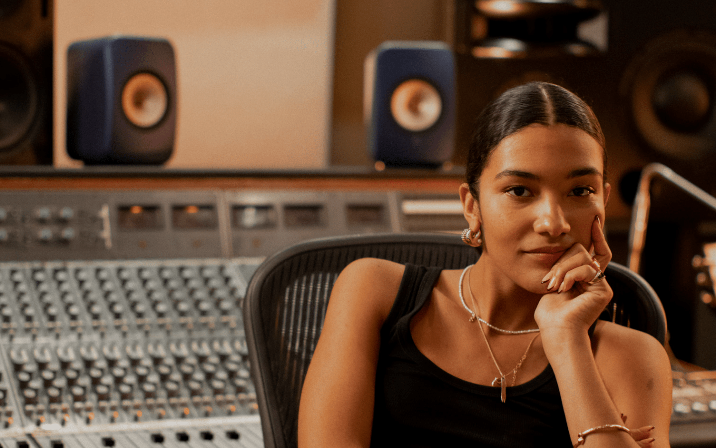Olivia Dean sitting in a recording studio surrounded by music equipment, headphones on, focused on creating new tracks.