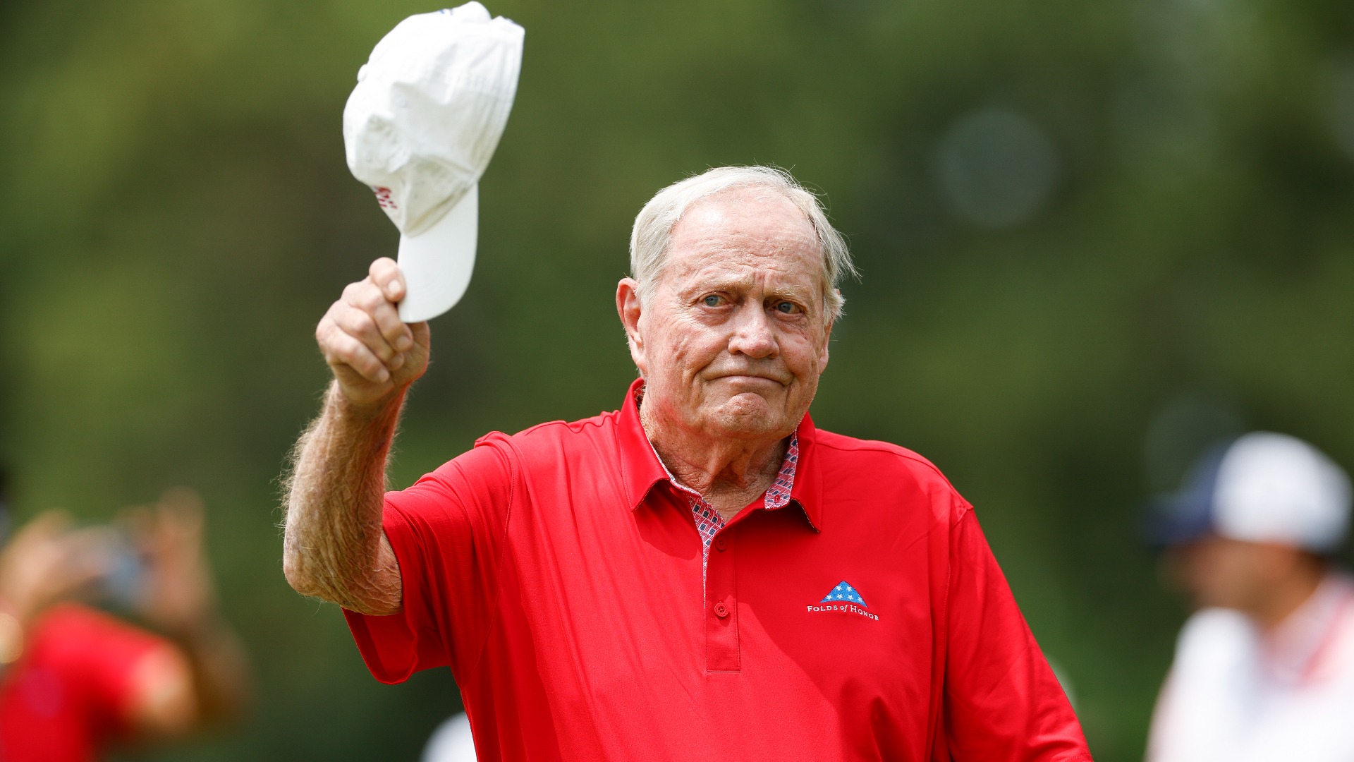 Jack Nicklaus removing his hat and waving to a cheering crowd, showing gratitude and connection with fans at a recent public appearance.
