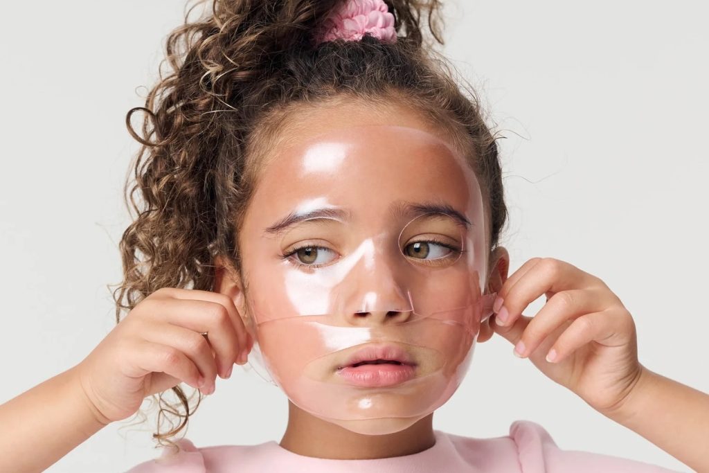 A young girl with a cheerful expression applying an animal-themed rini sheet mask, embodying joyful and safe kids' skincare innovation.