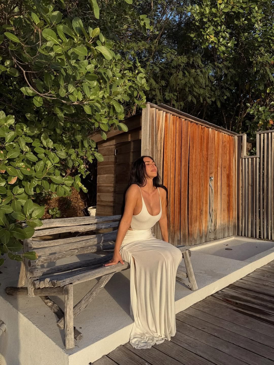 Kim Kardashian sitting on a bench in a white dress, soaking up the sun and gazing thoughtfully at the horizon on bar exam results day.