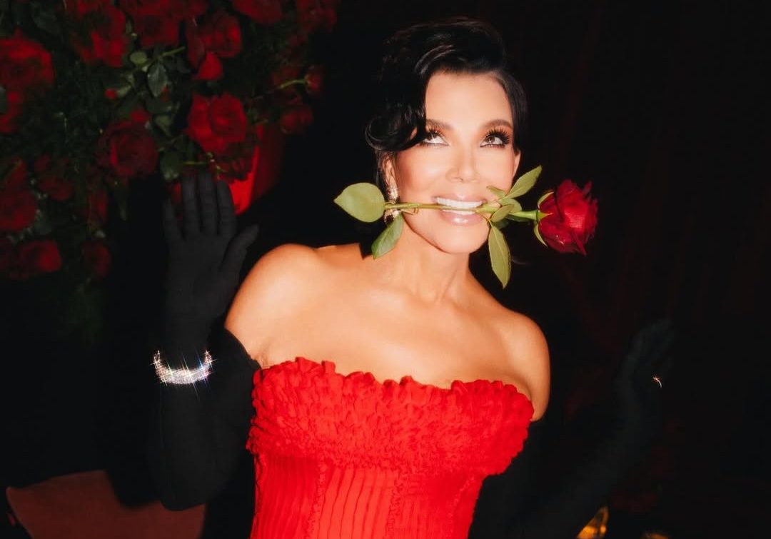 Kris Jenner channels her inner Bond girl as she poses with a red rose in her mouth, exuding glamour and confidence in a stunning red gown at her 70th birthday party.
