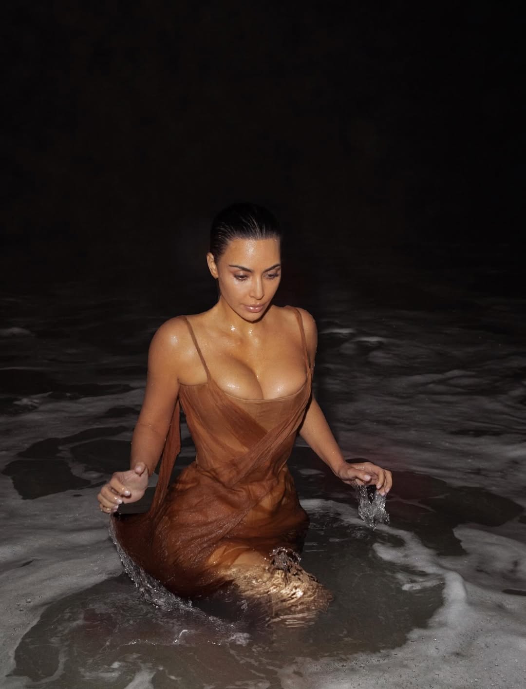 Kim Kardashian standing in the Rio ocean at night, shivering and bracing against the cold water while wearing a sheer Alexander McQueen gown.