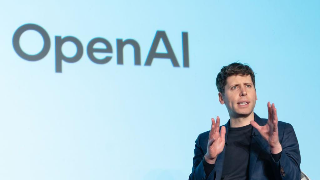 Sam Altman delivering a speech with the OpenAI logo displayed on a screen behind him.