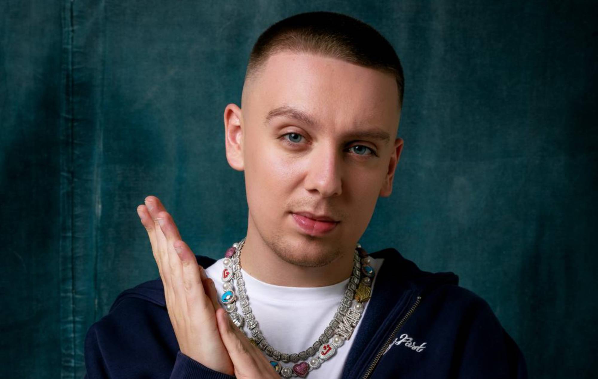 Rapper Aitch smiling and posing confidently during a photoshoot for his latest album.