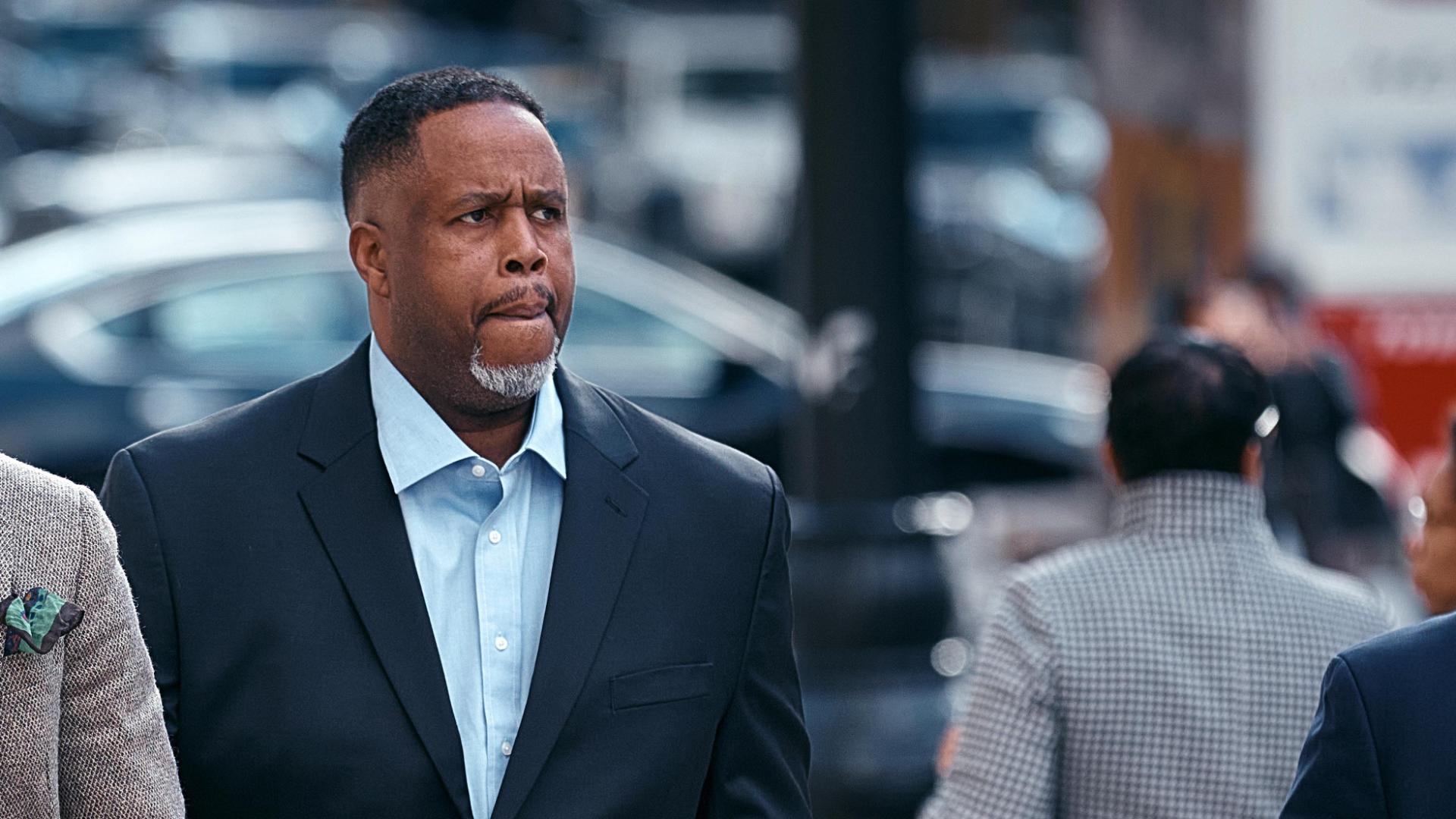 Damon Jones leaving the courthouse wearing a suit after pleading not guilty, looking serious as photographers capture the moment.