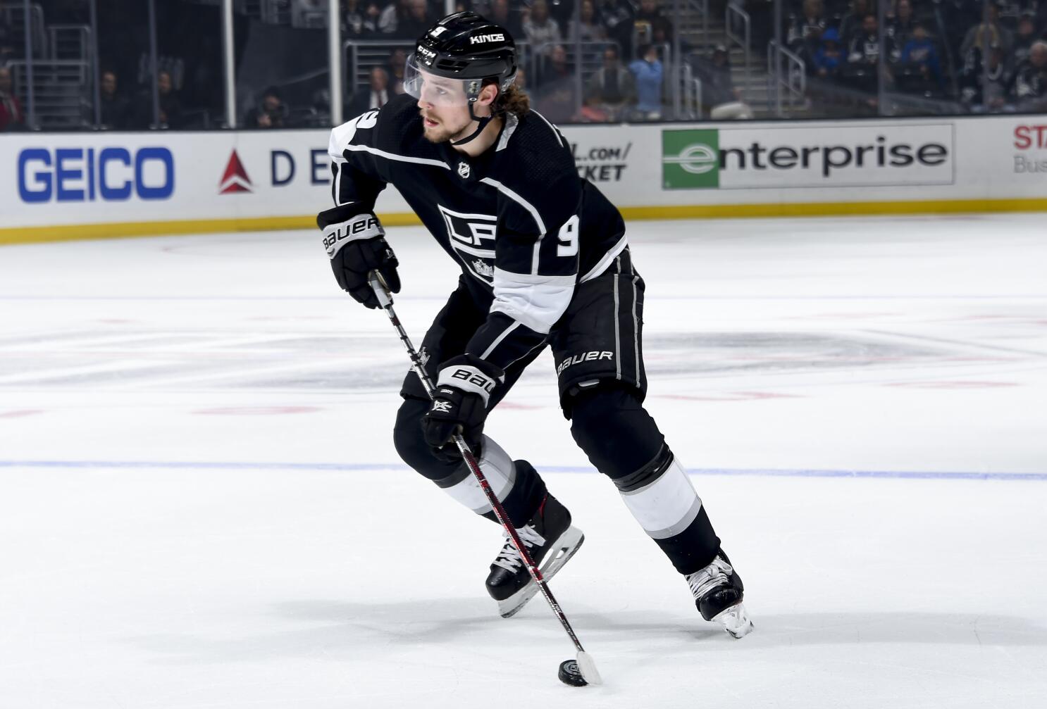 Adrian Kempe taking a powerful shot on the ice wearing a black Los Angeles Kings jersey during a game.