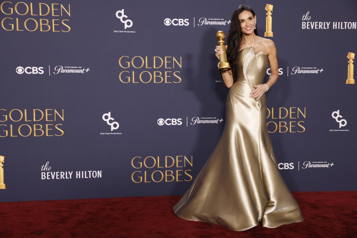 Demi Moore posing on the Golden Globes red carpet, holding her award and smiling for photographers.