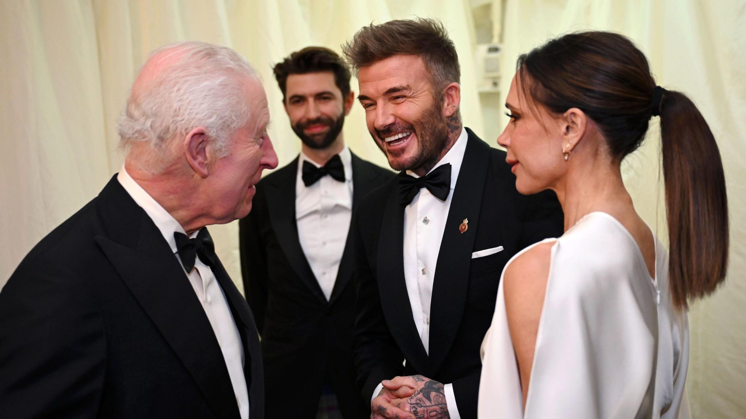 David and Victoria Beckham chatting with King Charles at a recent royal event, smiling and engaged in conversation.