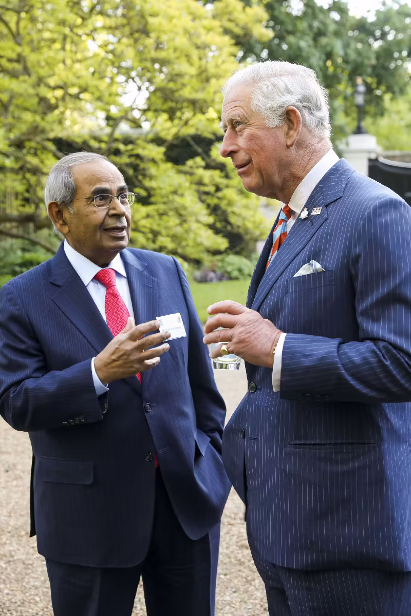 Gopichand Hinduja speaking with King Charles in the gardens of Buckingham Palace, both engaged in conversation during a formal event