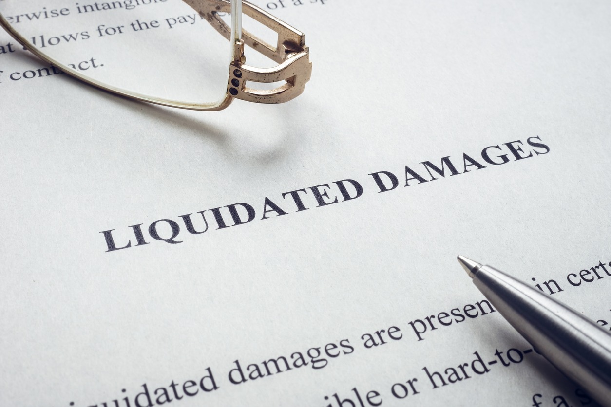 documents about liquidated damages with pen and glasses.