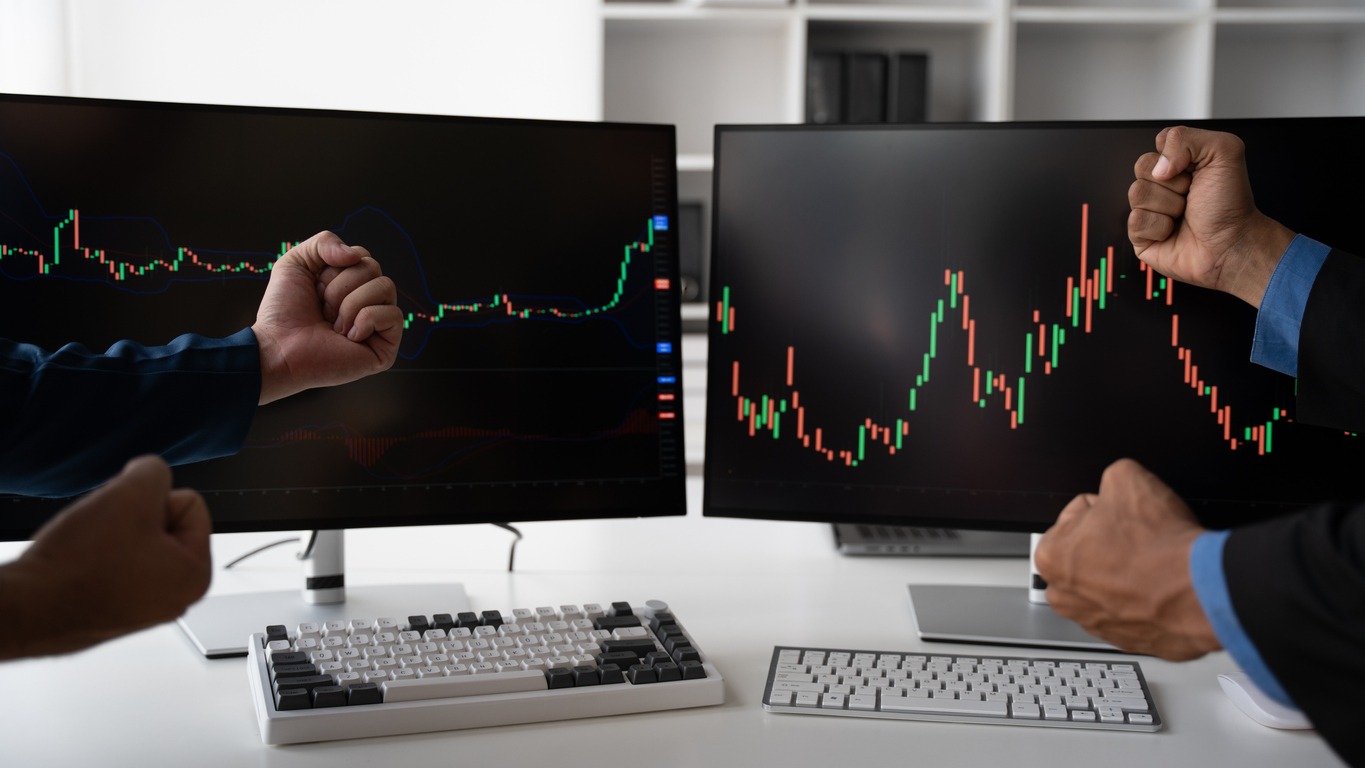 broker look at computer screen and do winner gesture celebrating successful trade in stock market working in modern office.