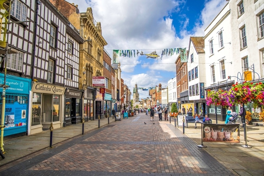 A busy UK high street lined with small independent shops, cafés, and local businesses, all preparing for and anxiously awaiting the upcoming Budget announcement.
