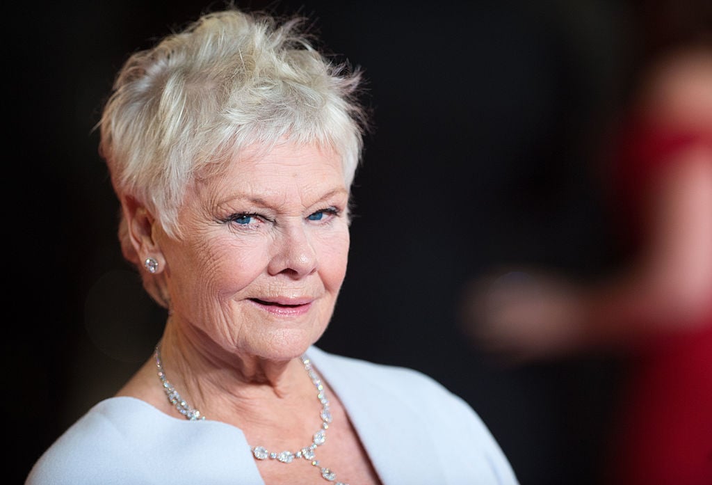 Dame Judi Dench smirking confidently at the camera while posing on the red carpet, dressed elegantly for the event.