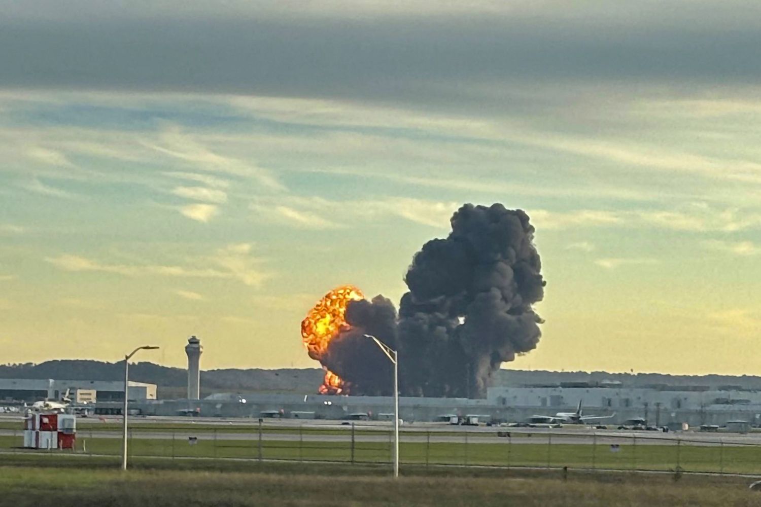 A dramatic aerial view captures a massive fireball erupting from a UPS MD-11 cargo plane moments after takeoff, as it skids off the runway and crashes into nearby industrial buildings at Louisville Muhammad Ali International Airport, sending thick plumes of black smoke billowing into the evening sky on November 4, 2025.