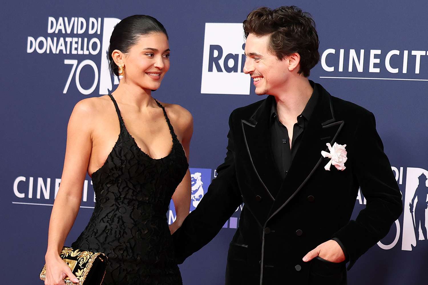 Kylie Jenner and Timothée Chalamet dressed in glamorous attire, smiling together on the red carpet at a high-profile event.