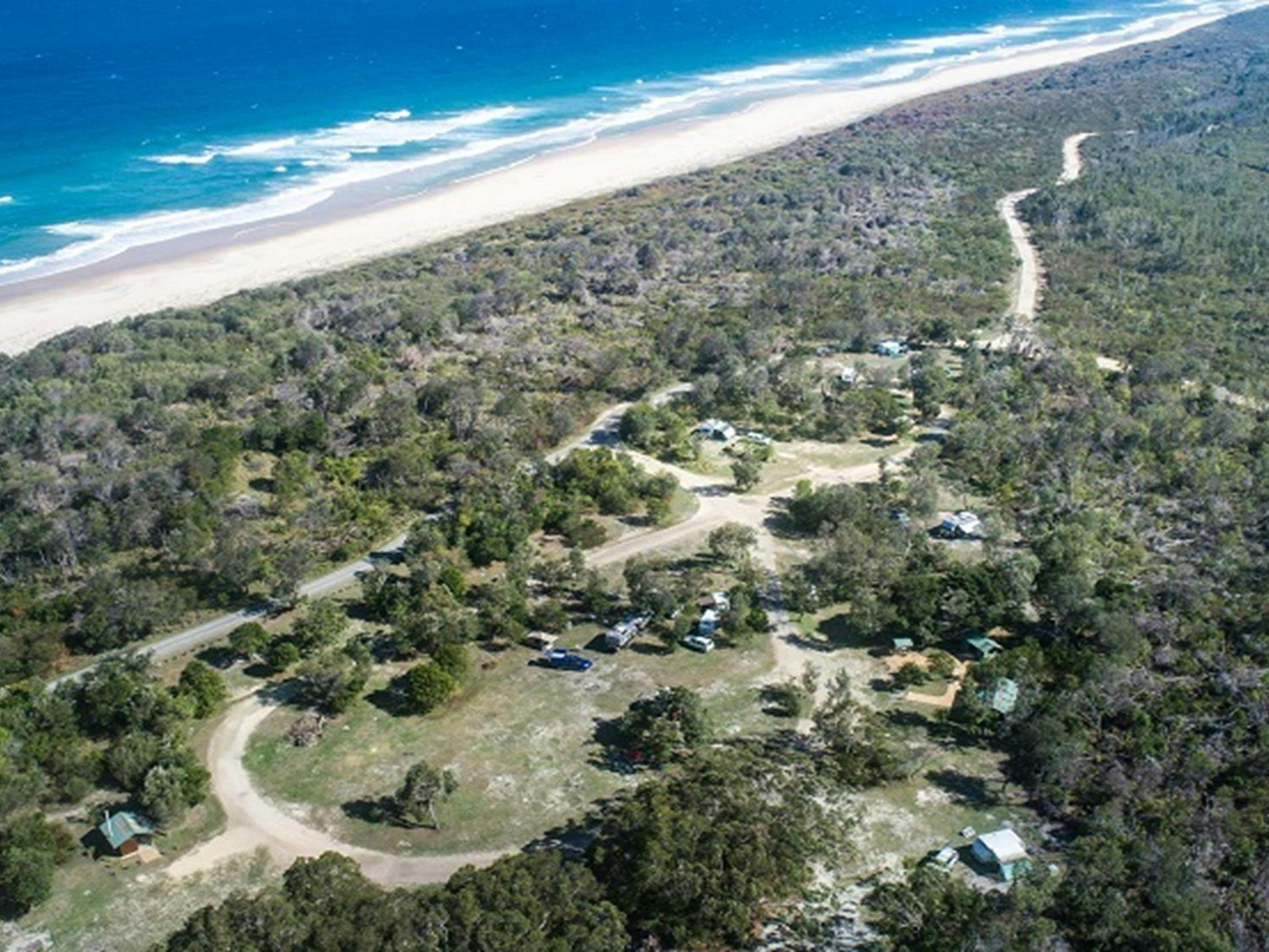 Aerial view of Kylies Beach in New South Wales, showing long stretches of isolated shoreline, rolling waves, and dense coastal bushland surrounding the sand.