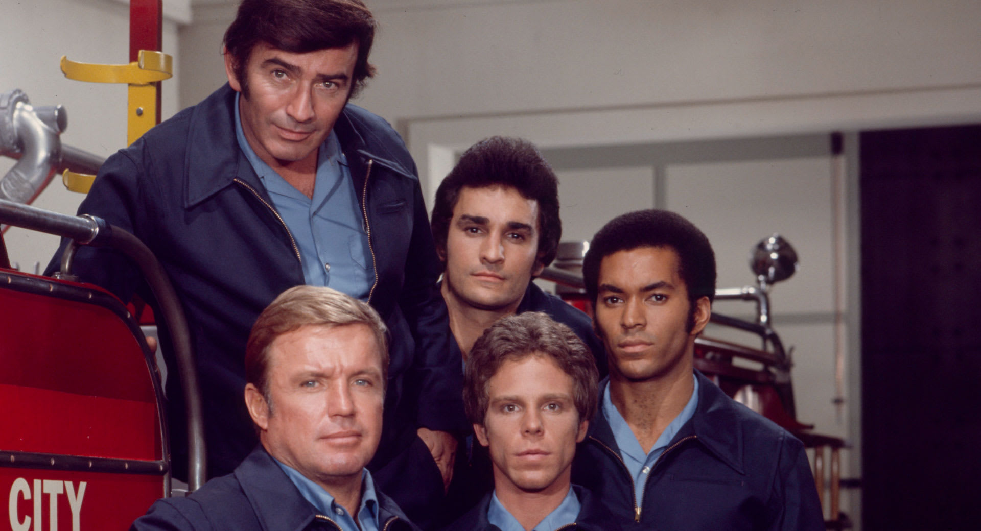 Michael DeLano as Johnny Venture on Rhoda, smiling as he performs in a firehouse setting.