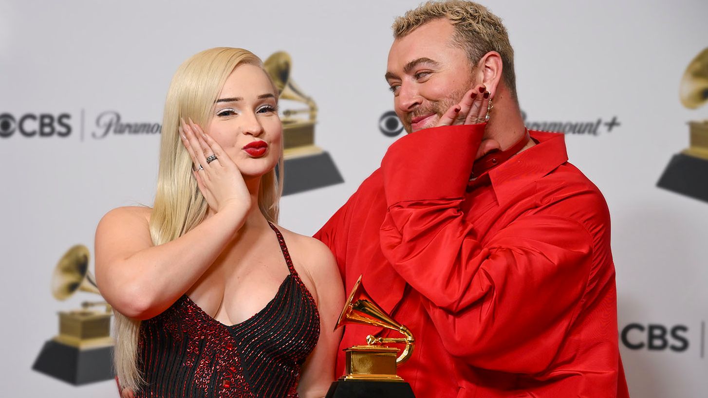 Sam Smith and Kim Petras pose together on the red carpet, smiling and holding a Grammy Award.