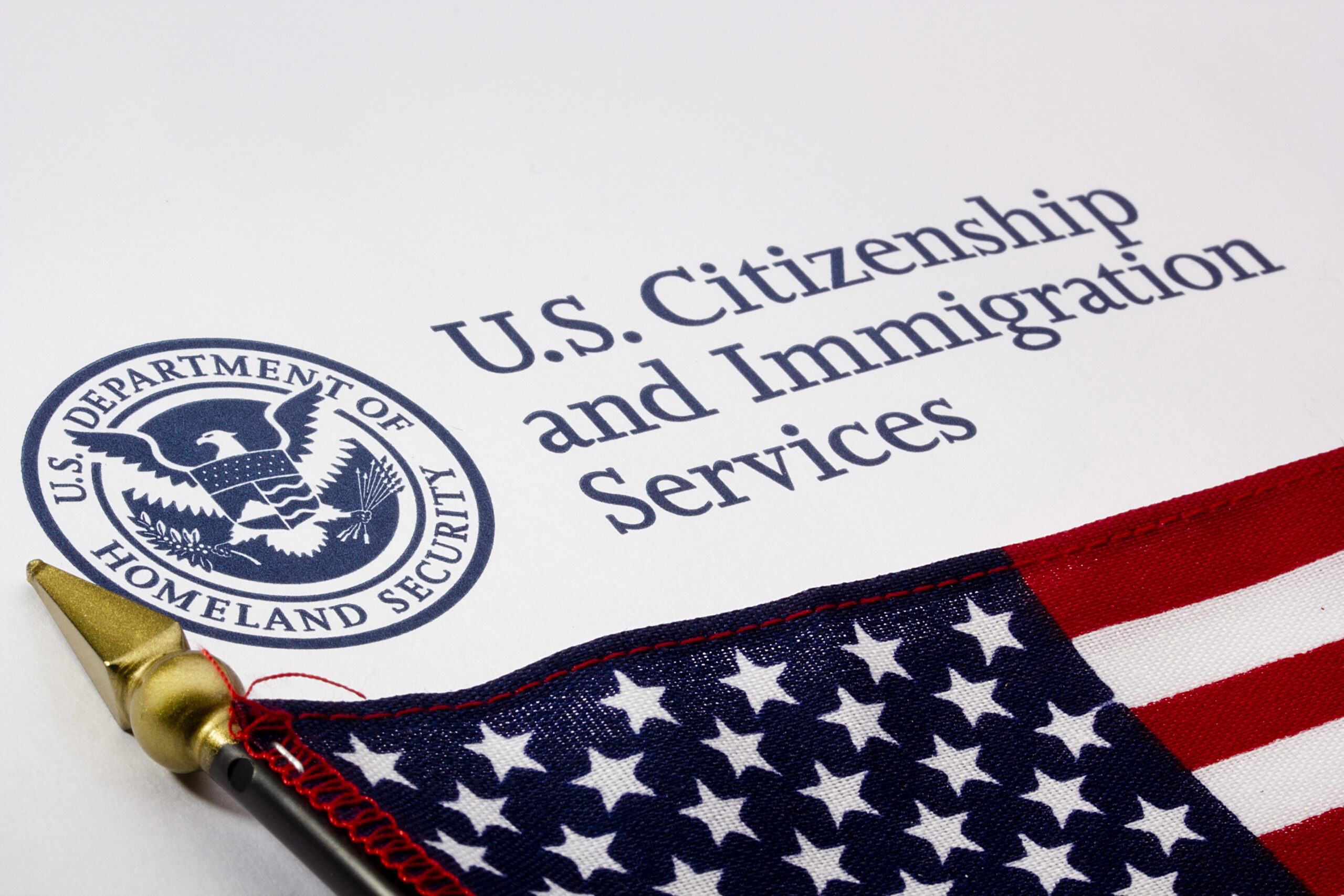 A close-up photograph of a U.S. immigration document resting beneath a folded American flag, symbolizing federal authority and shifting national immigration policies.