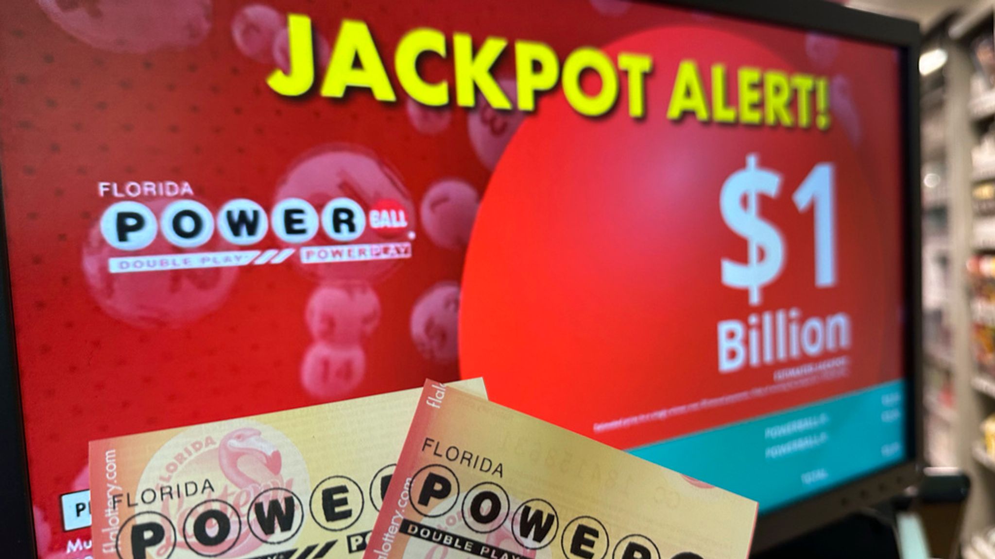 Powerball numbers displayed on a screen as a person holds two lottery tickets.