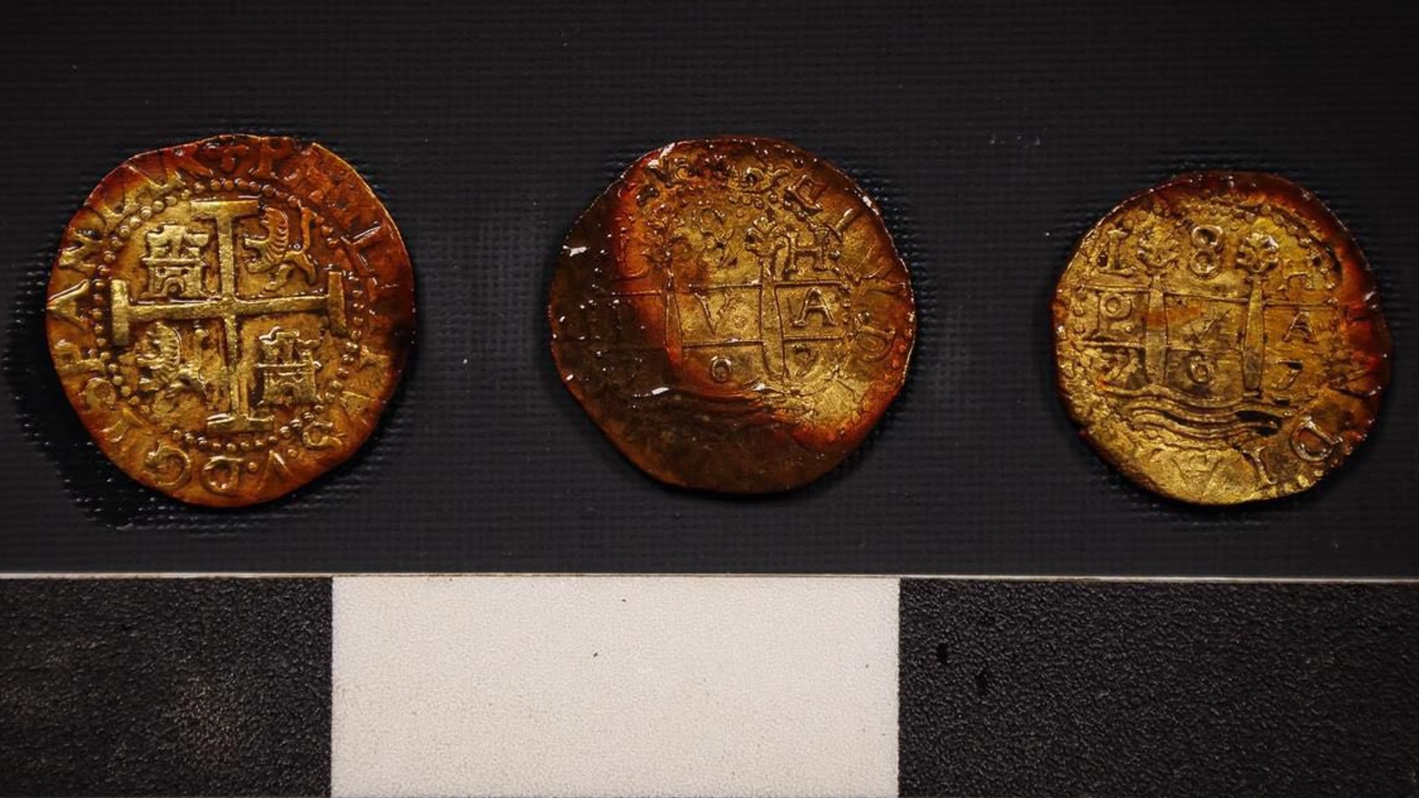 Close-up image of the three gold coins recovered from the San José shipwreck, showing their engraved details and preserved surfaces.