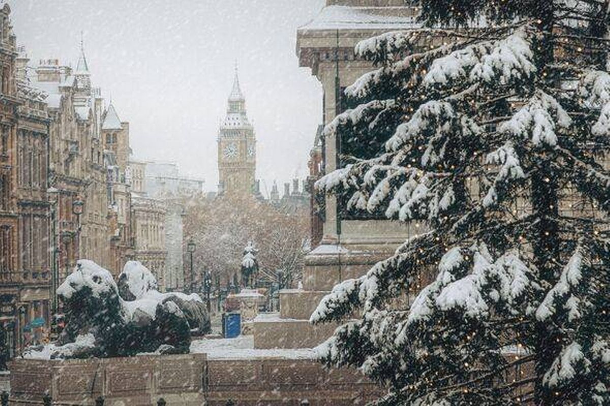 Big Ben and the Houses of Parliament dusted with Christmas snow, overlooking the River Thames as snowflakes fall over a festive London winter scene.