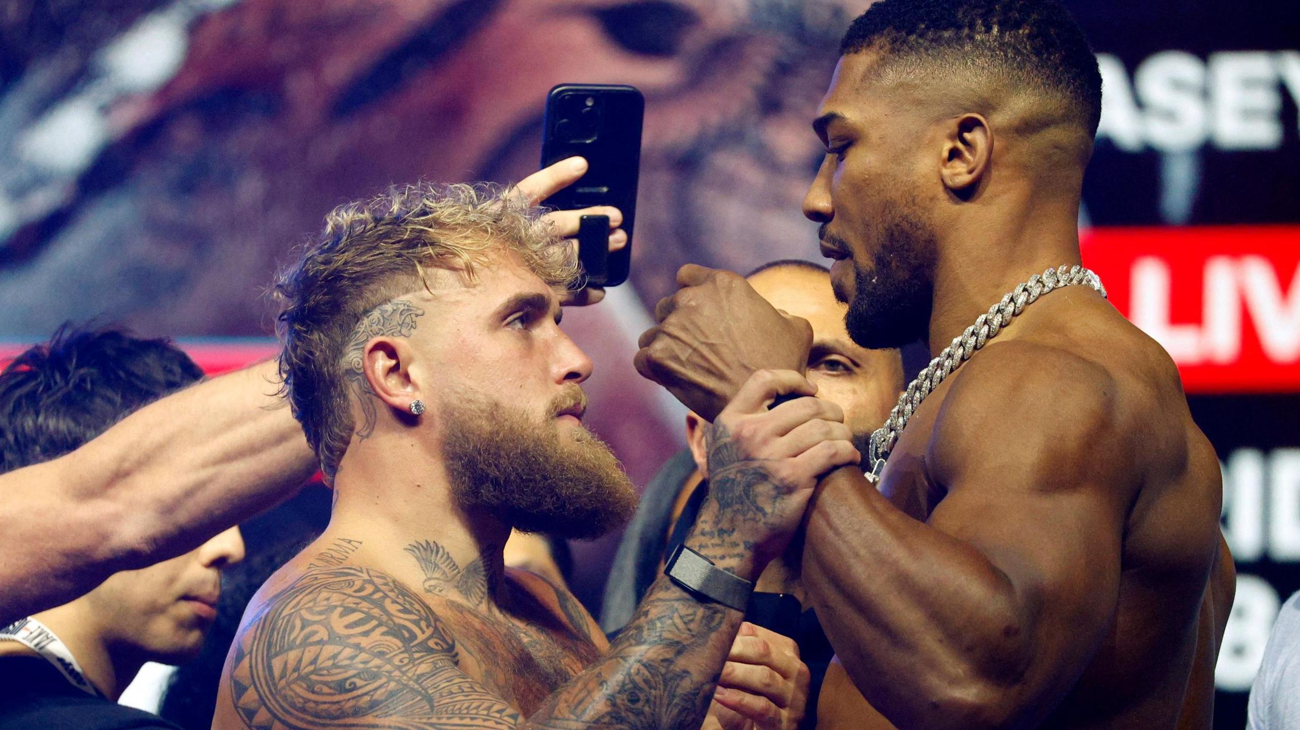 Jake Paul and Anthony Joshua facing off during a pre-fight stare-down, tense and ready for their December 19 boxing match.