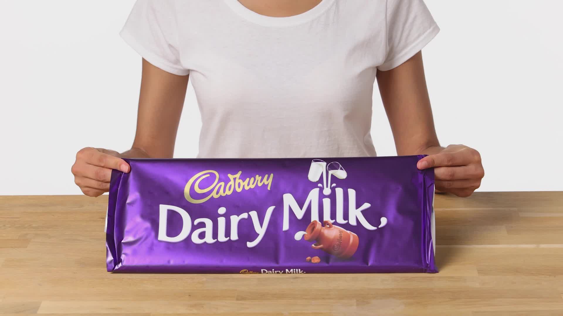 Person holding a Cadbury Dairy Milk bar, showing the smaller size of the chocolate in their hand amid rising prices and shrinkflation concerns.
