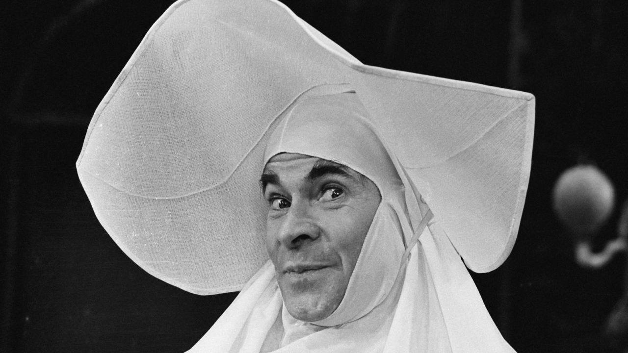 Black and white photo of Stanley Baxter in elaborate fancy dress, performing a character role on stage.