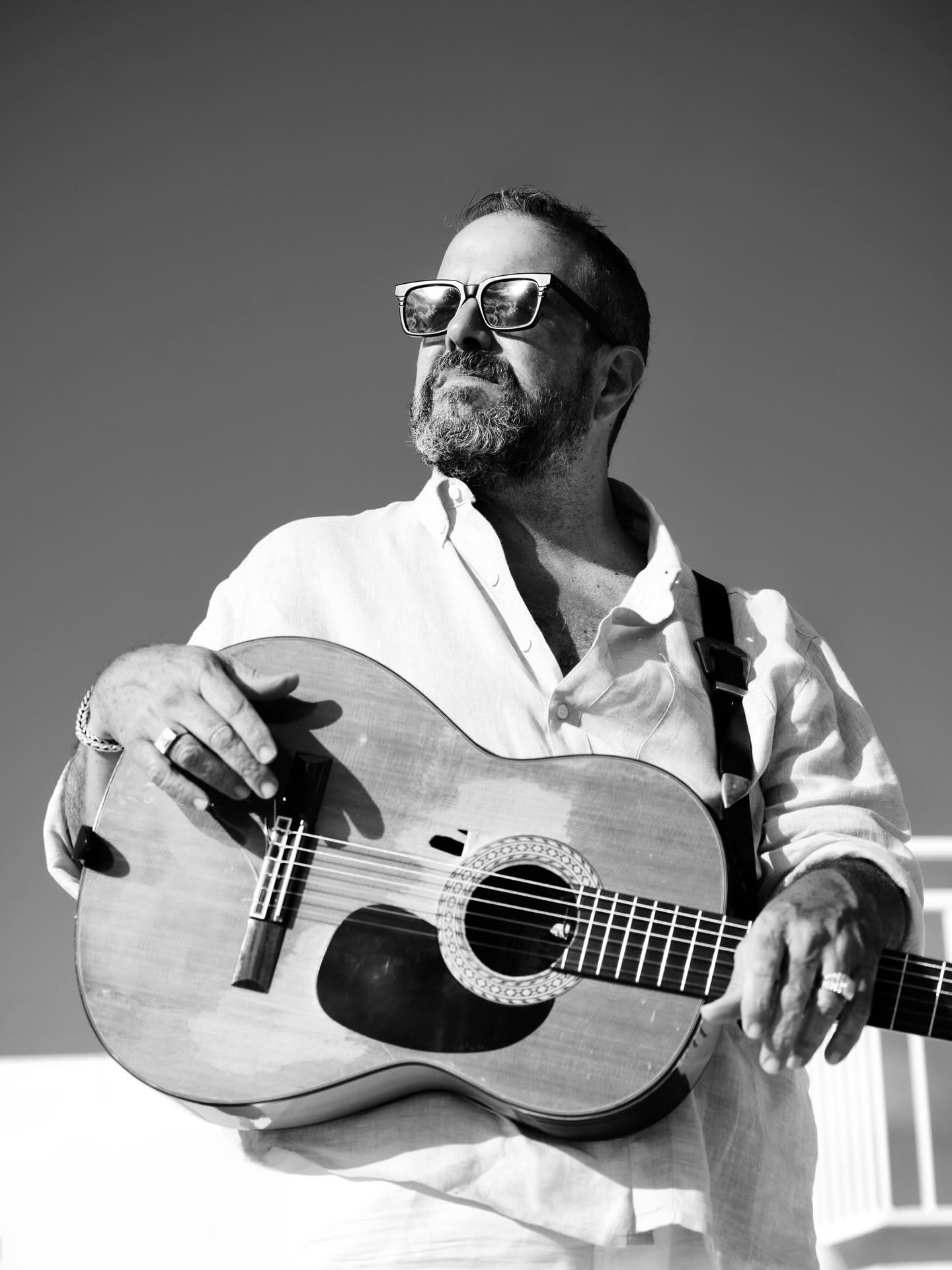 Black and white photo of Raul Malo posing with a guitar, looking thoughtfully into the distance.