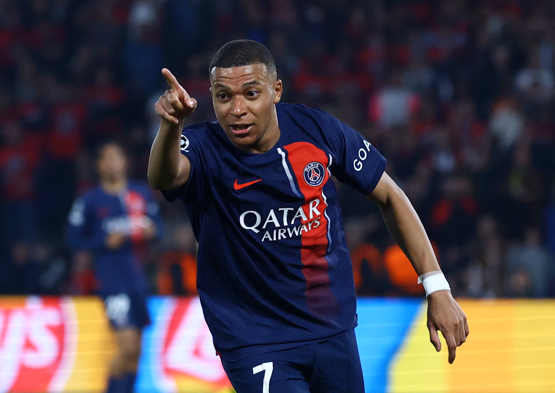 Kylian Mbappé pointing to the crowd after scoring a goal for Paris Saint-Germain, celebrating with fans in the stadium.