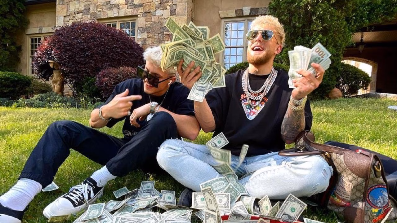 A younger Jake Paul sitting outside his mansion a few years ago, surrounded by stacks of cash, showcasing his early wealth and flashy lifestyle.