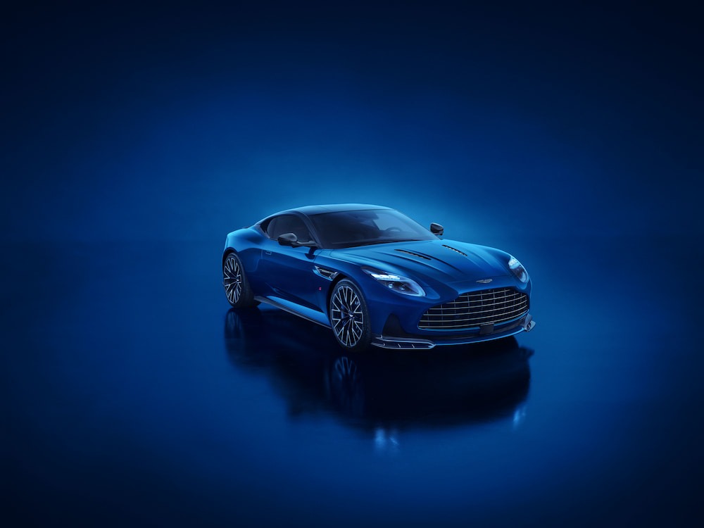 Aston Martin DB12 S parked against a neon blue illuminated backdrop, highlighting its sharp aerodynamic lines, aggressive front splitter and quad-tailpipe rear design.